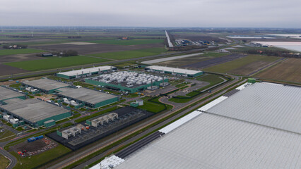 Aerial view of rows of industrial green buildings and containers under a cloudy sky, Agriport, Middenmeer, Netherlands.