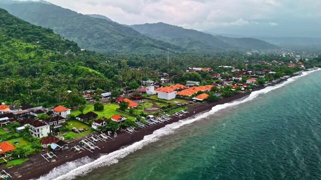 A coastal village with black sand beach, fishing boats, and lush hills along Bali&rsquo;s shoreline. Bali, Indonesia