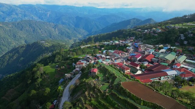 High gliding aerial over the dense town of Atok, Benguet, featuring vibrant rooftops and the majestic blue mountain ranges of the Cordillera.
