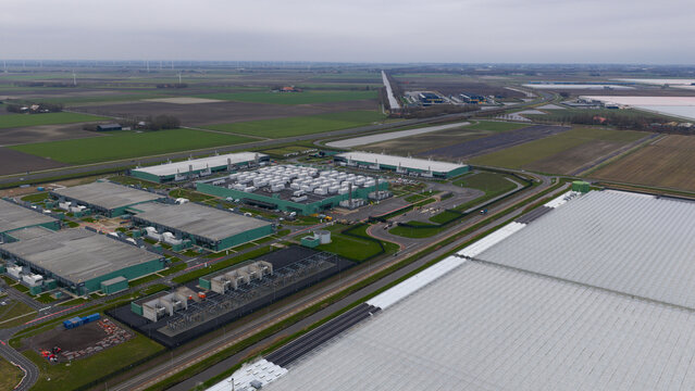 Aerial view of rows of industrial green buildings and containers under a cloudy sky, Agriport, Middenmeer, Netherlands. - Powered by Adobe