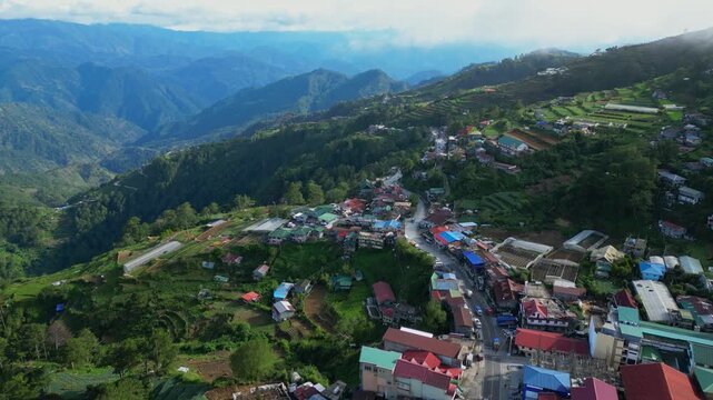 Sweeping turning glide aerial over the winding mountain highway, showcasing the dense roadside town and vibrant tiered terraces of Atok, Benguet, Philippines