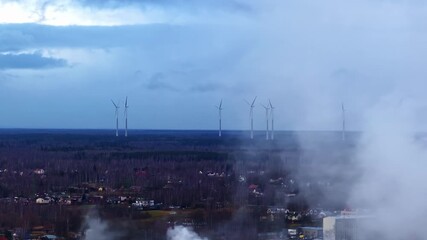 Drone tracks left past drifting smoke to reveal wind turbine field emphasizing shift toward renewable power