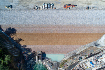 Lee Valley, New Zealand - 15 September 2021: Aerial view of the dam's textured layers cascading down to meet the river, where turquoise water contrasts with the stark concrete structure.