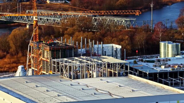 Aerial drone reveals large data center construction site with steel frames, cranes, and active industrial work, early morning sun illumination, establish