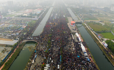 Dhaka, Bangladesh - 25 December 2025: Aerial view of a vast throng of people gathered along the Purbachal Expressway, flanked by canals, under a hazy sky.