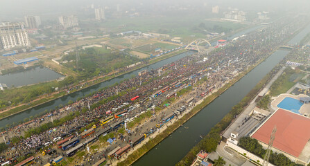 Dhaka, Bangladesh - 25 December 2025: Aerial view of a bustling Purbachal Expressway, teeming with crowds and vibrant buses alongside serene waterways, under a hazy sky.