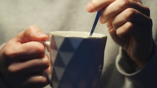 A close-up of a beautiful cup with a hot drink inside.
A person stirs tea in a glass with a teaspoon.