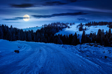 winter landscape with snow covered country road winding through fir forest in mountains at night. alpine countryside of in full moon light. inner strength to overcome fear, loneliness in darkness