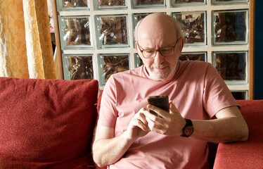 Senior man relaxing on sofa using smartphone