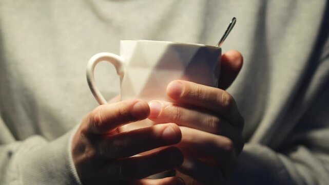 A teacup and spoon in a glass.
Hot tea in a glass.
A man warms himself holding a cup of hot tea in his hands.