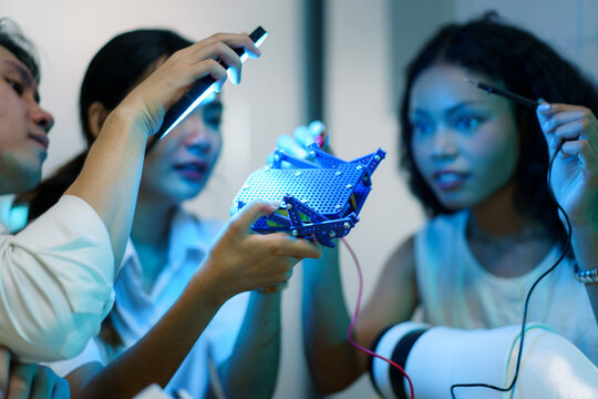 Engineering students testing robotic hand prototype with electronic tools