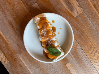Rolled crepe topped with toasted meringue, caramel sauce and mint leaf, served on a white plate over a wooden table in warm natural light. Amazing dessert in restaurant or cafe © Avalepsap