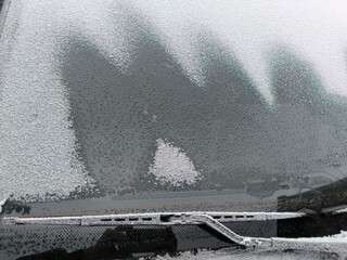 The frozen windshield of the car begins to thaw with drops of water, frozen wiper blades