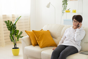 Woman talking on smartphone on white sofa in modern living room. Home communication, remote...