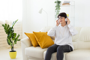 Woman listening to music with headphones on sofa in modern living room. Audio relaxation, digital entertainment, and mindful leisure through home technology.