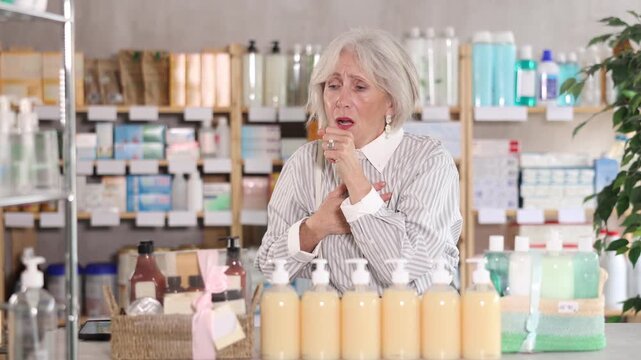 Elderly woman buyer with cough choosing medicines and hygiene products in pharmacy