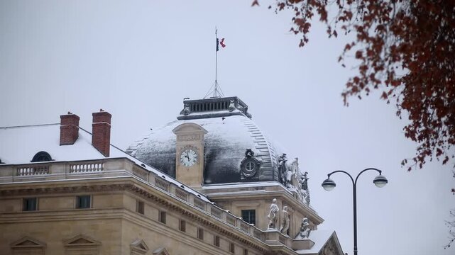 Snow-covered Ecole Militaire with French flag on dome in Paris during winter.