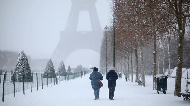 People walking through heavy snowfall on Champ de Mars near the Eiffel Tower in Paris. Snowstorm covers the scene in a wintery haze, creating a magical and atmospheric view of the city