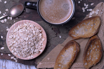 Black mug with coffee foam on tree bark, with a bowl of rolled oats and crispy toasted bread, rustic style