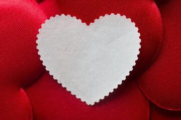 Creative mockup for wedding invitation or romantic note. Clean white paper label in heart shape with copy space lying on bright red silk texture. Vintage mail concept. Photo