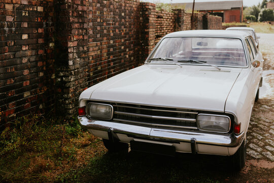 Vintage white car parked beside a weathered brick wall