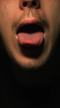 Expression with tongue in mouth.
A man opens his mouth and shows his tongue sticking out against a dark background.