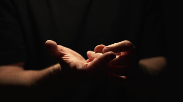 A man in a dark room bends his fingers and counts something.
A man counts arguments by bending his fingers on a palm.