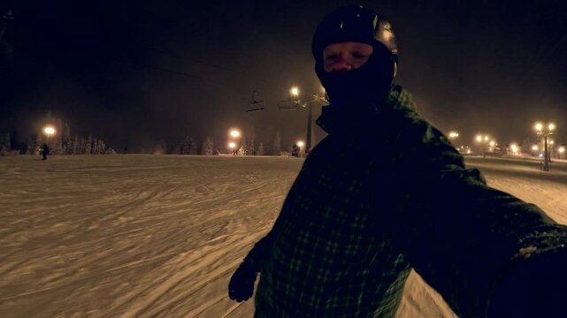 Snowboarder rides down a snowy slope at night under bright lights