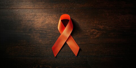 Orange ribbon placed on dark wood surface symbolizing awareness efforts, focus on visual contrast and communication