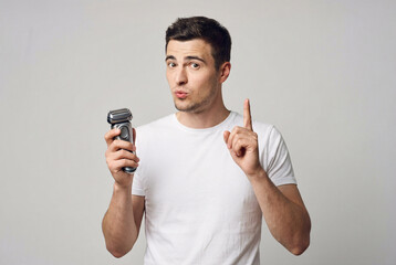 Young man holding electric shaver and raising finger with warning expression on neutral background, representing grooming advice, personal care caution and shaving tips concept.
