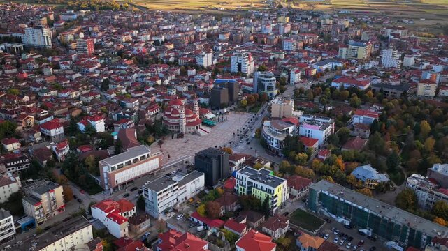 Aerial video of Kor&ccedil;&euml; featuring the main square, the Orthodox Cathedral, dense urban housing and mountain scenery in warm evening light.