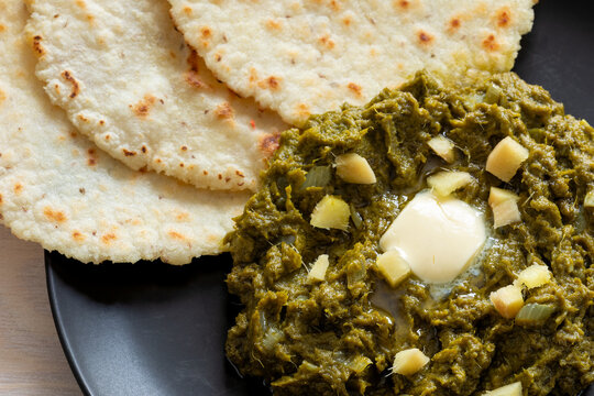 Close-up of mustard greens puree with butter, ginger, and cornmeal flatbreads on the second table. Punjabi Sarson ka saag served with butter, ginger, and makki ki roti. 