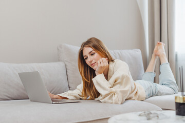 Freelance student working from home on a laptop while relaxing on a couch in the afternoon light