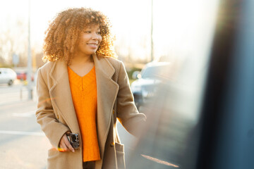 Happy young woman smiling, opening car door in city during golden hour sunlight