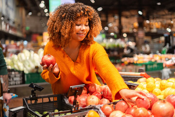 Smiling woman shopping for fresh pomegranates in a supermarket produce aisle