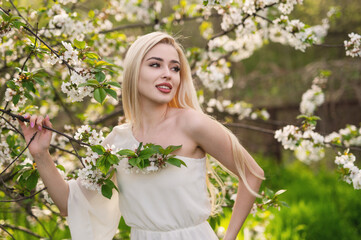 A beautiful girl with long blond hair in a blooming garden, a portrait among branches of apricot and cherry blossoms. Spring is the blossoming of femininity, beauty, and peace.