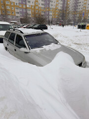 A car is parked in a snowdrift. Heavy snowfall, frost and blizzard in the city. Problem of transport in winter.