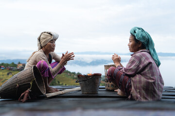 Two Asian rural women sitting together on a wooden platform