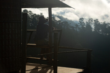 Naklejka premium Silhouette of a person resting on a wooden balcony overlooking misty mountains