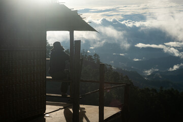 Naklejka premium Silhouette of a person resting on a wooden balcony overlooking misty mountains
