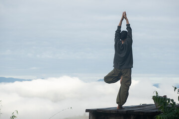 Person practicing yoga tree pose on a wooden platform above clouds