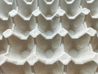 A top-down, close-up view of an empty grey molded pulp egg tray, showing a repetitive geometric pattern and textured paper surface.