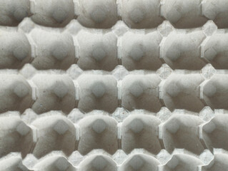 A top-down, close-up view of an empty grey molded pulp egg tray, showing a repetitive geometric...