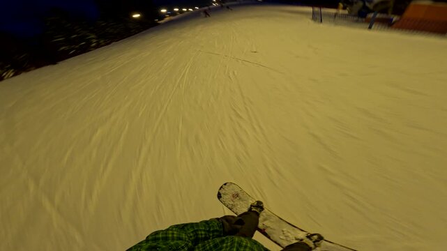 Snowboarding at night on a lit slope with clear tracks