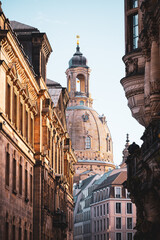 The Frauenkirche dome is visible between buildings in Dresden. The scene is set during a clear day, highlighting the church tower against the sky.