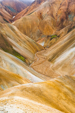 View of a majestic tableau unfolds, where ochre and cream-colored mountains converge, carved by a meandering stream, in the otherworldly landscape, Landmannalaugar, Central Highland, Iceland.