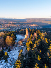 Stepanka lookout tower stands tall in the Jizera Mountains as the sun sets. The snow-covered ground and trees surround the tower. Visitors enjoy the scenery from the lookout area.