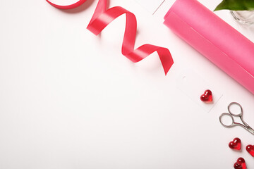 Gift wrapping accessories with pink ribbon, paper, scissors, red hearts on white background. Flat lay for Valentine's Day or Mother's Day. Copyspace.