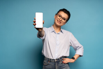 Portrait of gorgeous woman demonstrate smartphone display empty space isolated on blue color background