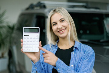 Saleswoman showing calculator and explaining car cost in dealership
